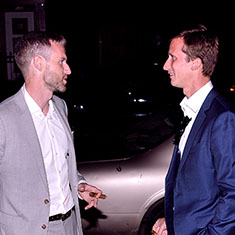 Groom and friend outside wedding reception smoking cigars