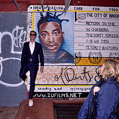 Friend posing in front of a wall of graffiti with bride watching